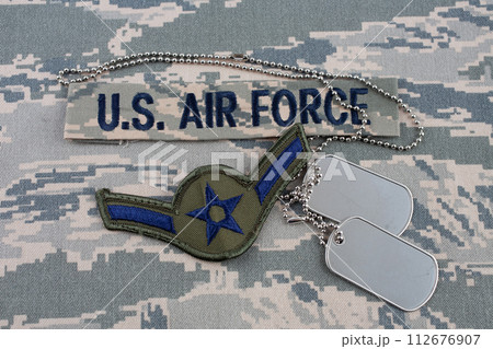US AIR FORCE branch tape and Airman rank patch and dog tags on digital tiger-stripe pattern Airman Battle Uniform (ABU) background US AIR FORCE branch tape and Airman rank patch and dog tags on digital tiger-stripe pattern Airman Battle Uniform (ABU) background 112676907