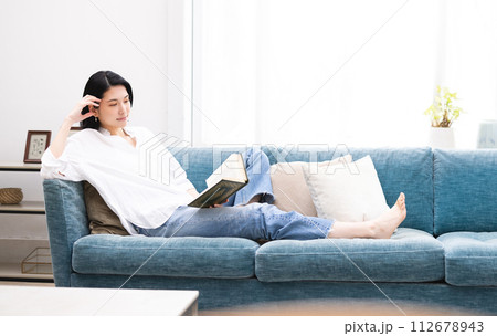 リビングでくつろぎながら読書をする若い女性 112678943