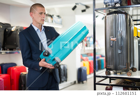 Confident man in a store carefully examines a travel suitcase 112681151