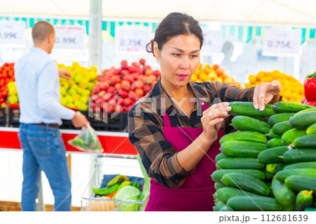 Female greengrocery owner preparing fruits and vegetables for sale on counter Female greengrocery owner preparing fruits and vegetables for sale on counter 112681639