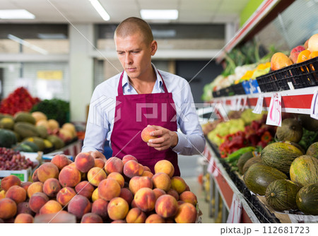 Seller laying out fruits and vegetables on shelves in grocery store 112681723