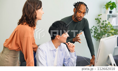 オフィスでパソコンを見ながら会話する多国籍の人々 112682010