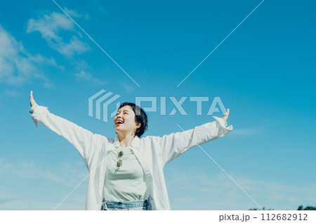 笑顔で青空の下で大きく手を広げているショートカットのおしゃれな女性 112682912