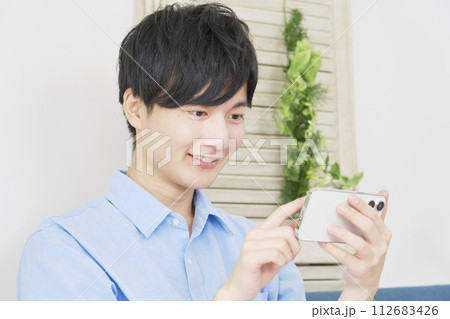 リビングルームでスマホを横向きで使う若い男性 リビングルームでスマホを横向きで使う若い男性 112683426