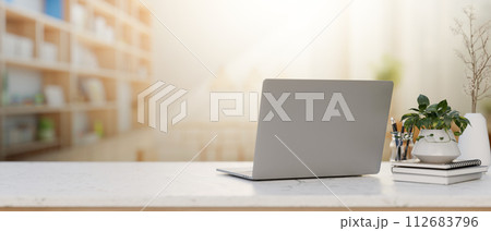 A laptop computer, decor, and space on a white table with a blurred background of a bright library. A laptop computer, decor, and space on a white table with a blurred background of a bright library. 112683796