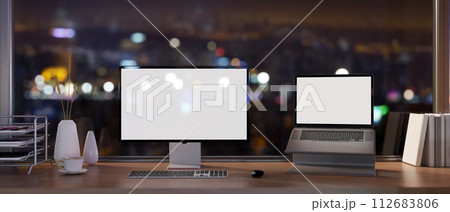 A modern skyscraper office at night with a computer and white-screen laptop mockup on a desk. A modern skyscraper office at night with a computer and white-screen laptop mockup on a desk. 112683806
