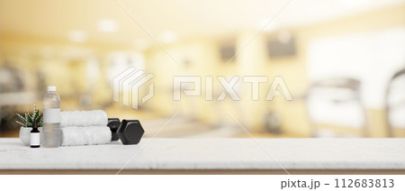 A presentation space on a white table features a dumbbell, towels, and a water bottle in a fitness. A presentation space on a white table features a dumbbell, towels, and a water bottle in a fitness. 112683813