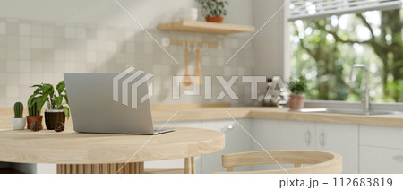 A back view image of a laptop computer on a wooden dining table in a minimalist neutral kitchen. A back view image of a laptop computer on a wooden dining table in a minimalist neutral kitchen. 112683819