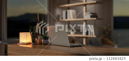 A contemporary home office workspace at night features a laptop computer on a wooden desk. 112683825