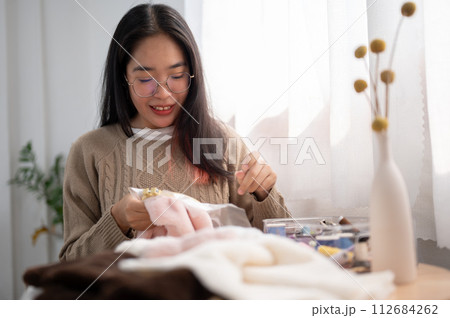 A focused young Asian woman threading a pattern on an embroidery frame, hand-sewing on cloth. 112684262