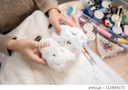 A close-up image of a woman crafting a fluffy plush toy by hand at home. 112684273