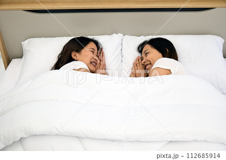 Two young Asian couple women lying Sharing a Joyful Moment in Bed Two young Asian couple women lying Sharing a Joyful Moment in Bed 112685914