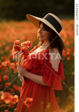 Woman poppy field red dress hat. Happy woman in a long red dress in a beautiful large poppy field. Blond stands with her back posing on a large field of red poppies. 112690214