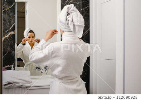 Woman wrapped her hair in towel after shower looking in mirror Woman wrapped her hair in towel after shower looking in mirror 112690928