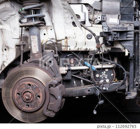 The front part of the car after an accident in a car repair service with a disassembled hood and metal grille and various parts in the garage box. 112692765