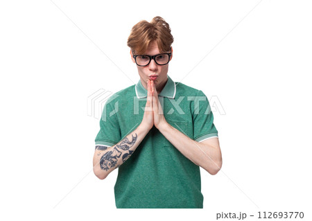 young red-haired man in a green t-shirt folded his hands in anticipation on a white background with 112693770