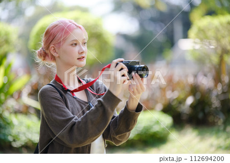 Beautiful Young artist Woman taking photo in flowers garden. Young cute girl carry the camera in the garden. 112694200