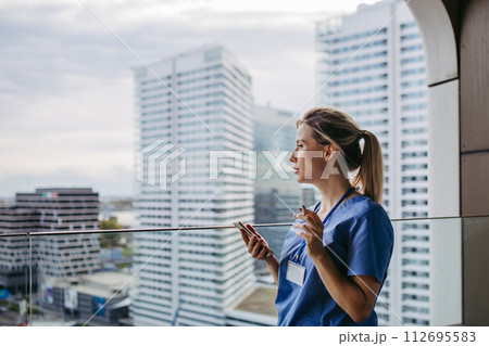 Nurse smoking cigarette at balcony after work. Doctor feeling overwhelmed at work, taking break. Stresfull at hospital, clinic. 112695583