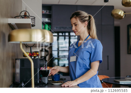 Female nurse or doctor getting ready for work in the morning, making coffee and preparing breakfast. Work-life balance for healthcare worker. 112695585