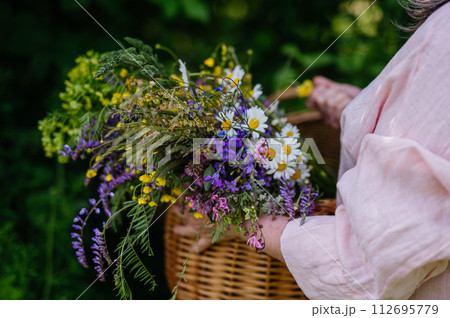 Woman holding wicker basket with meadow flowers. A colorful variety of summer wildflowers. Woman holding wicker basket with meadow flowers. A colorful variety of summer wildflowers. 112695779