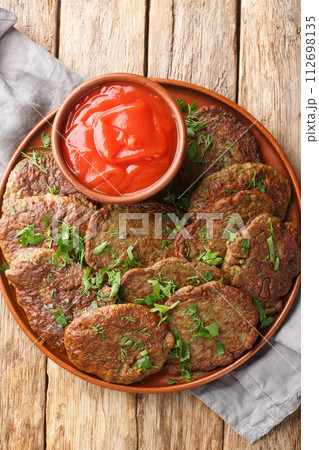Delicious beef liver patties served with tomato sauce close-up in a plate. Vertical top view 112698135