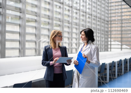 Doctor talking to pharmaceutical sales representative, presenting new pharmaceutical product. Hospital manager talking with doctors team. 112698469