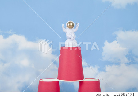 a white astronaut figurine with gold helmet on a pyramid of red paper cups 112698471