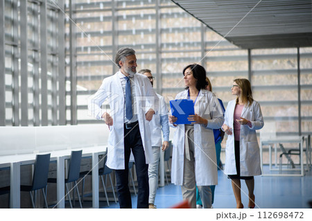 Team of doctors discussing test results, walking across corridor. Colleagues discussing patients diagnosis. 112698472