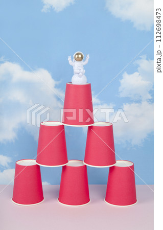 a white astronaut figurine with gold helmet on a pyramid of red paper cups a white astronaut figurine with gold helmet on a pyramid of red paper cups 112698473