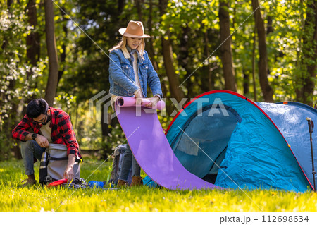 Woman in a straw hat rolling a mat near the tent 112698634