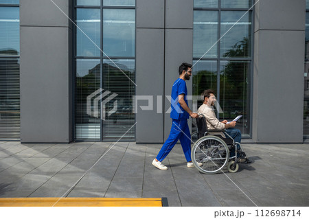 Male nurse taking a disabled patient on a wheelchair for a walk Male nurse taking a disabled patient on a wheelchair for a walk 112698714