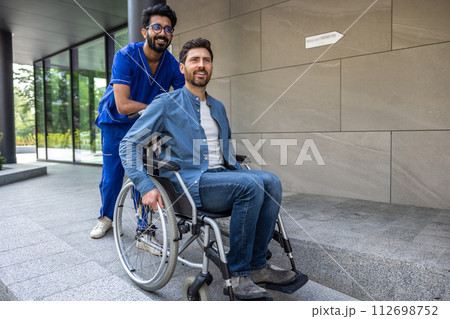 Young dark-haired male nurse taking a patient in wheelchair for walk 112698752