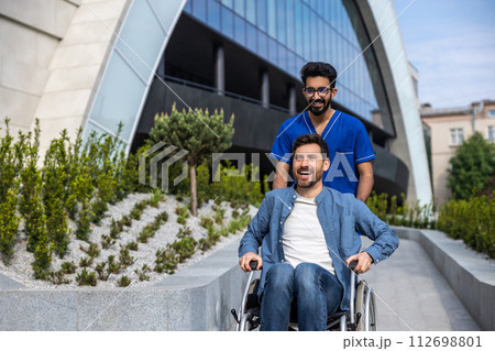Dark-haired male nurse taking a patient in wheelchair for a walk 112698801