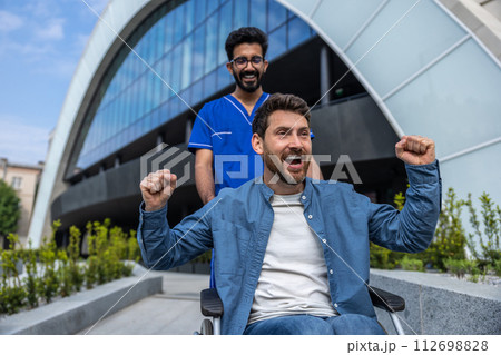 Young smiling bearded man in wheelchair having a walk with a nurse Young smiling bearded man in wheelchair having a walk with a nurse 112698828