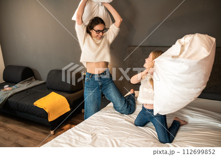 Mother and her little daughter playing with cushions on bed in hotel room 112699852