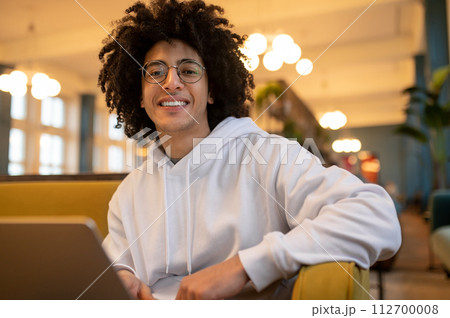 Young curly-haired man with laptop working in a hotel hall Young curly-haired man with laptop working in a hotel hall 112700008