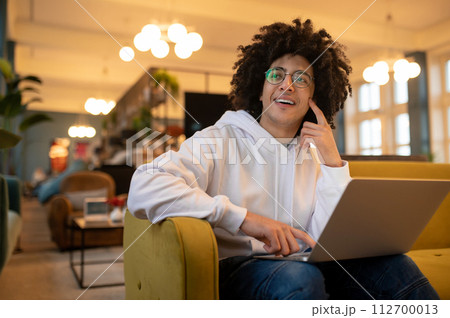 Young curly-haired man with laptop working in a hotel hall Young curly-haired man with laptop working in a hotel hall 112700013