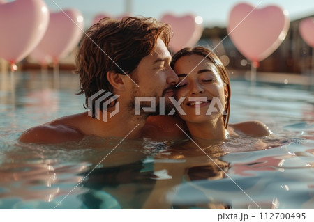 A couple in love is relaxing in a pool against a background of red balls in the form of hearts. Valentine's day A couple in love is relaxing in a pool against a background of red balls in the form of hearts. Valentine's day 112700495