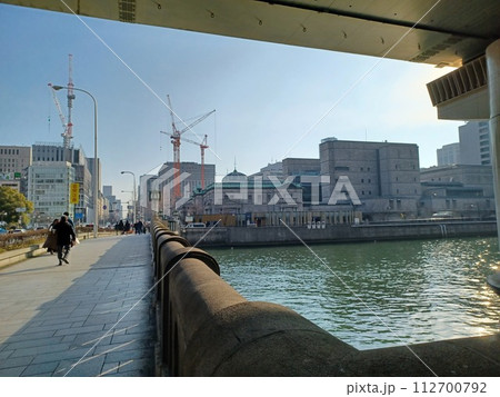 頭上に高速道路の高架橋、正面の青い屋根のレトロなビルの向こうに建設工事中の大型クレーン 頭上に高速道路の高架橋、正面の青い屋根のレトロなビルの向こうに建設工事中の大型クレーン 112700792