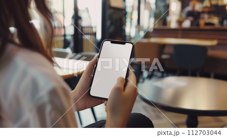 Mockup, woman's hands holding mobile phone with blank screen in coffee shop. Generative AI 112703044