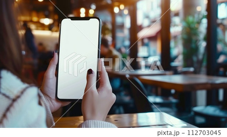 Mockup, woman's hands holding mobile phone with blank screen in coffee shop. Generative AI 112703045