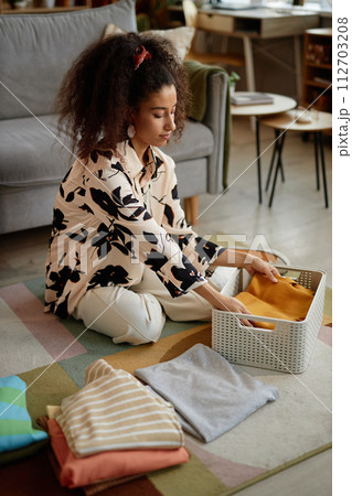 Full length portrait of young woman folding and sorting clean clothes on laundry day 112703208