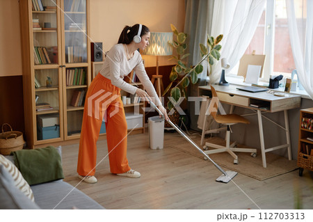 Full length portrait of young woman mopping floors and listening to music at home while enjoying cleaning copy space Full length portrait of young woman mopping floors and listening to music at home while enjoying cleaning copy space 112703313