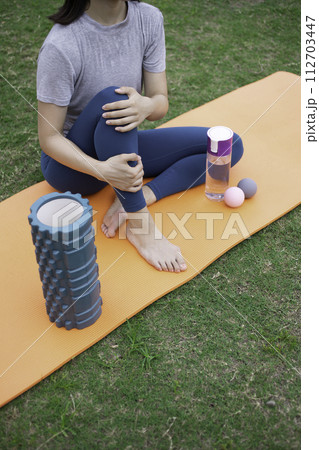 ヨガウェアを着て芝生の上でストレッチをする女性の足元 112703447