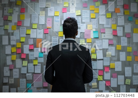 Back view of Businessman check week plan attached on big wall with paper notes. Generative AI Back view of Businessman check week plan attached on big wall with paper notes. Generative AI 112703448