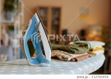 Close up background image of light blue iron on ironing board with stack of clothes copy space Close up background image of light blue iron on ironing board with stack of clothes copy space 112703459