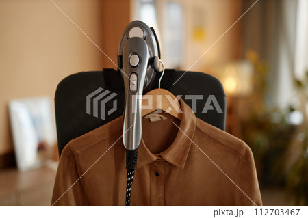 Close up of garment steamer appliance with clothes hanging on vertical ironing board copy space Close up of garment steamer appliance with clothes hanging on vertical ironing board copy space 112703467