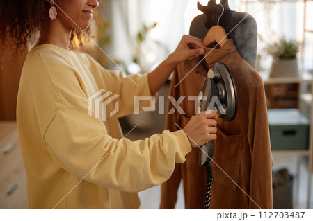 Side view closeup of smiling young woman using garment steamer on delicate velvet jacket copy space 112703487