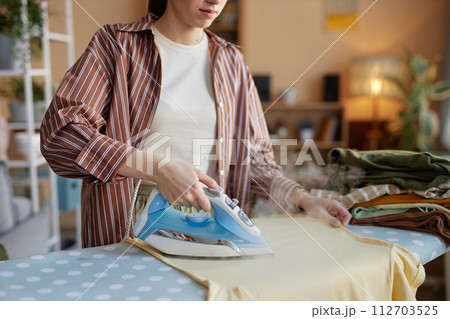 Close up woman ironing clothes on ironing board and taking care of house chores on laundry day copy space Close up woman ironing clothes on ironing board and taking care of house chores on laundry day copy space 112703525