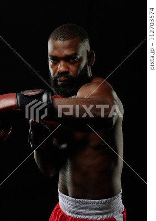 Vertical portrait of tough Black boxer looking at camera and practicing punches 112703574